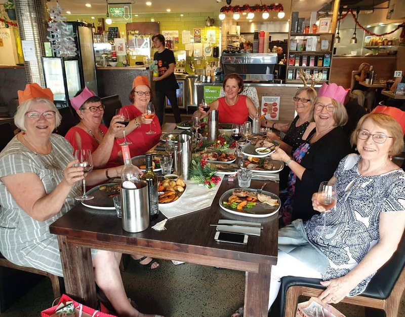 A group in Christmas cracker hats raising glasses around a long table
