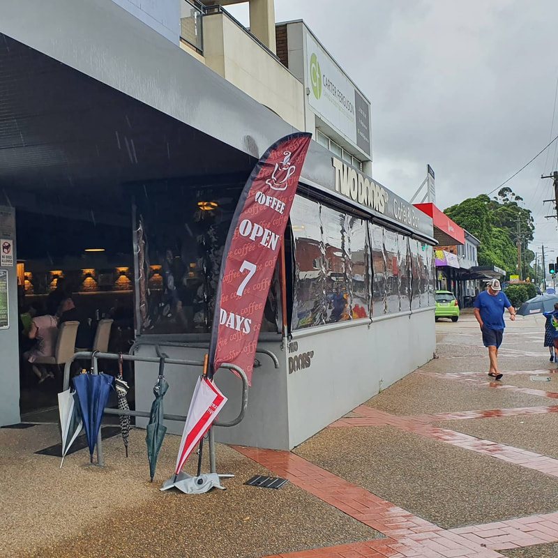 The Two Doors Up shopfront on the Princes Highway, Fairy Meadow, with an Open 7 Days flag